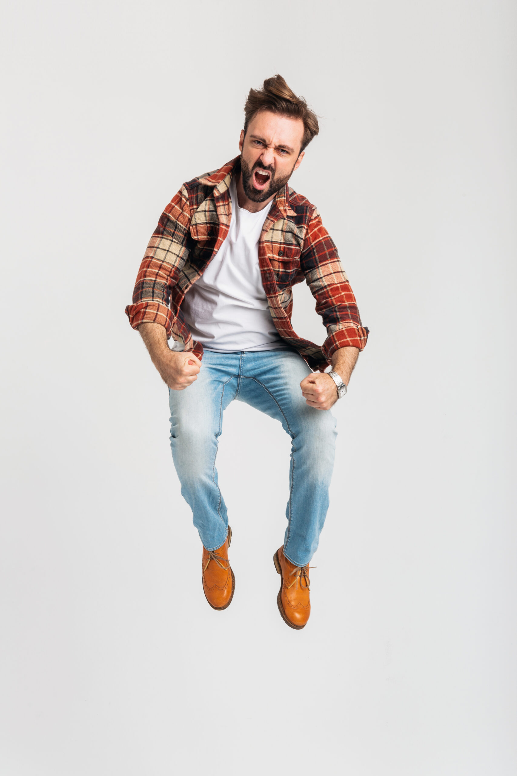 isolated handsome emotional strong bearded man active jumping in hipster outfit dressed in jeans and checkered shirt full length standing on white studio background, agressive angry emotion